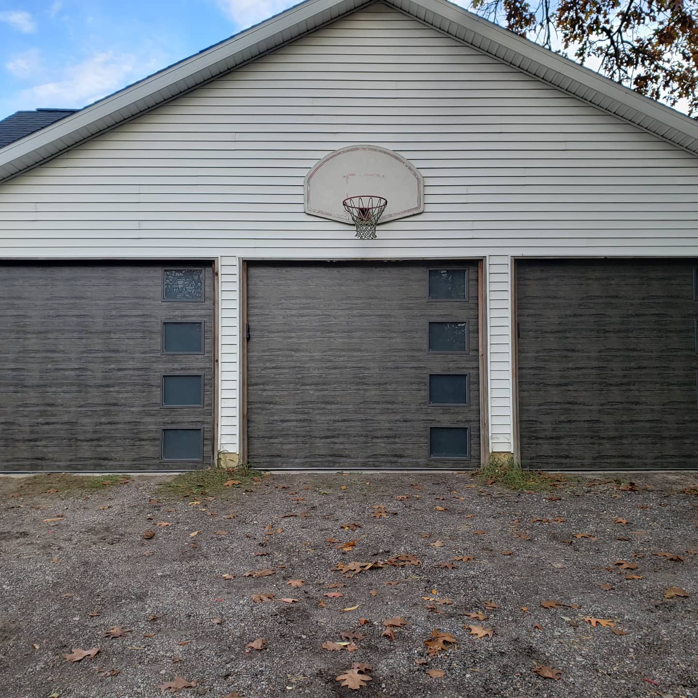 A three-car garage with a weathered basketball hoop mounted above the center door; fallen leaves scattered on the ground.