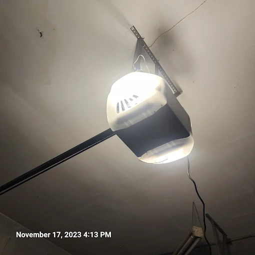 Ceiling-mounted garage door opener with a light turned on, attached to a metal track. Date and time stamp: November 17, 2023, 4:13 PM.