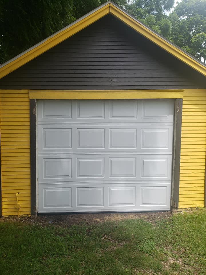 A yellow and black garage with a closed white garage door, surrounded by grass and trees.